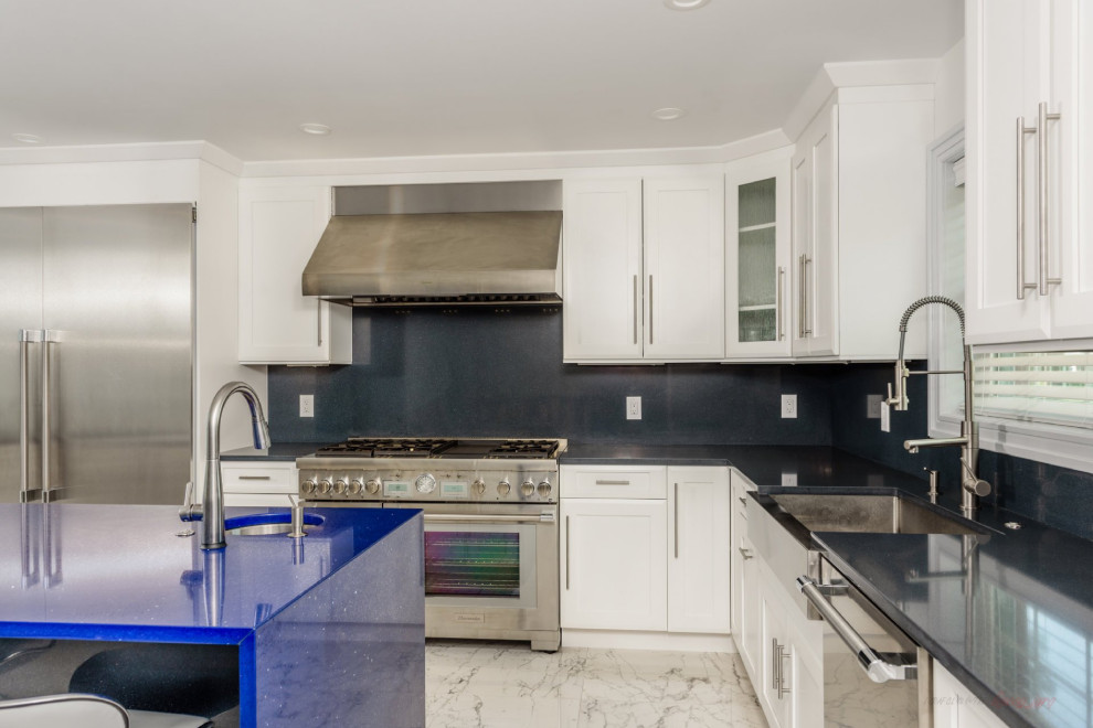 This is an example of a large modern l-shaped eat-in kitchen in New York with a farmhouse sink, recessed-panel cabinets, white cabinets, quartz benchtops, black splashback, engineered quartz splashback, stainless steel appliances, marble floors, with island, multi-coloured floor and blue benchtop.