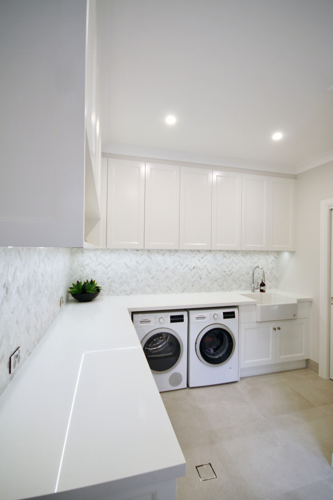 Inspiration for a large l-shaped utility room in Sydney with a belfast sink, recessed-panel cabinets, white cabinets, engineered stone countertops, grey splashback, marble splashback, grey walls, ceramic flooring, a side by side washer and dryer, grey floors and white worktops.