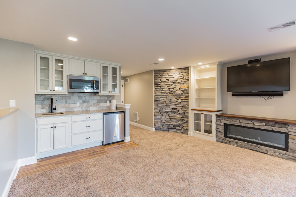 This is an example of a large transitional walk-out basement in Philadelphia with beige walls, carpet, a ribbon fireplace, a stone fireplace surround and beige floor.
