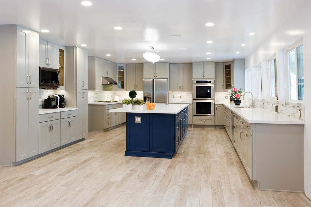 This is an example of an expansive contemporary u-shaped eat-in kitchen in Los Angeles with a drop-in sink, shaker cabinets, grey cabinets, quartz benchtops, multi-coloured splashback, glass tile splashback, stainless steel appliances, porcelain floors, with island, beige floor and white benchtop.