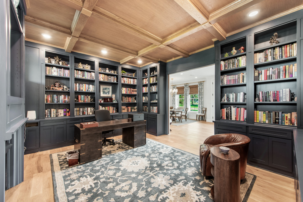 This is an example of a large transitional home office in Dallas with a library, blue walls, light hardwood floors, a standard fireplace, a wood fireplace surround, a freestanding desk, coffered and panelled walls.