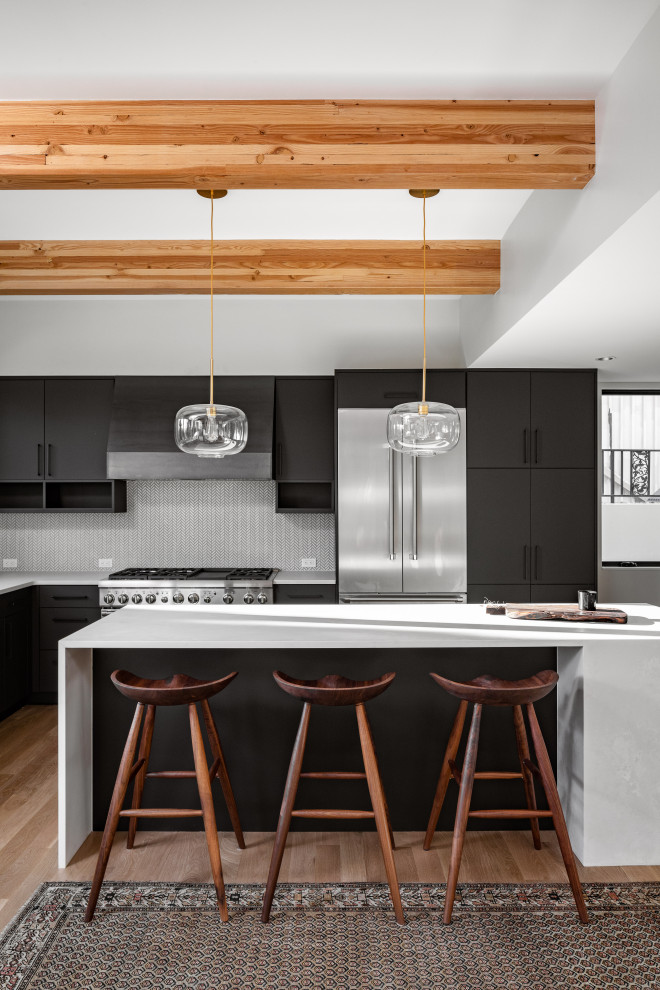 Example of a minimalist medium tone wood floor kitchen design in Denver with black cabinets, stainless steel appliances and an island