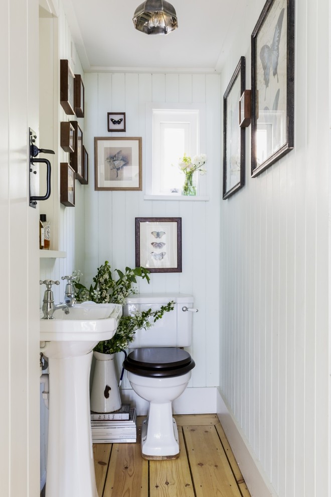 Small traditional powder room in Dorset with a one-piece toilet, white walls, light hardwood floors, a pedestal sink and beige floor.