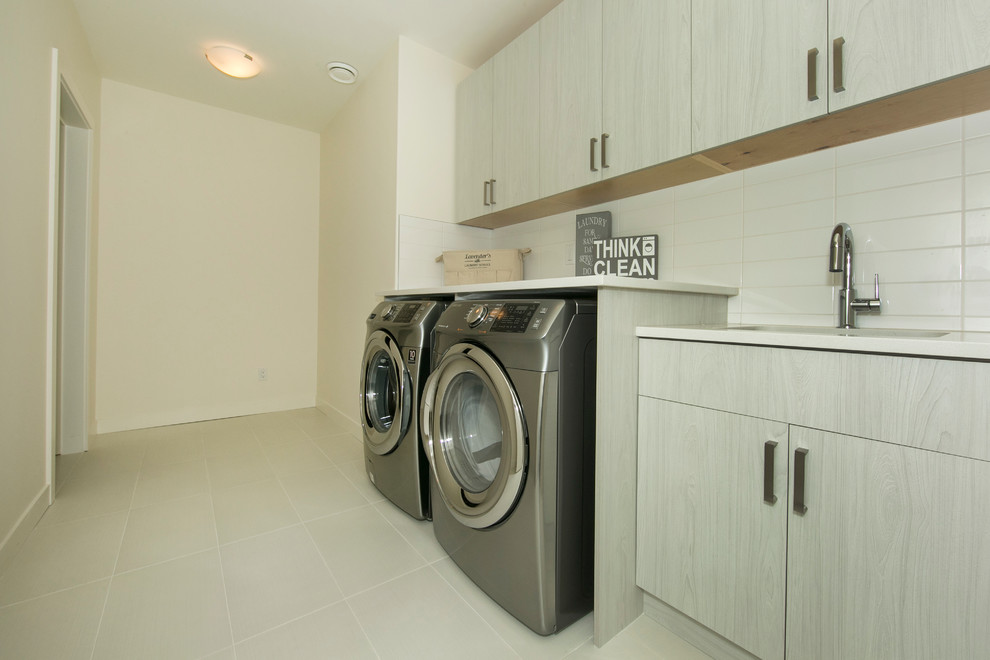 Large contemporary single-wall dedicated laundry room in Edmonton with an undermount sink, flat-panel cabinets, light wood cabinets, laminate benchtops, white walls, ceramic floors and a side-by-side washer and dryer.