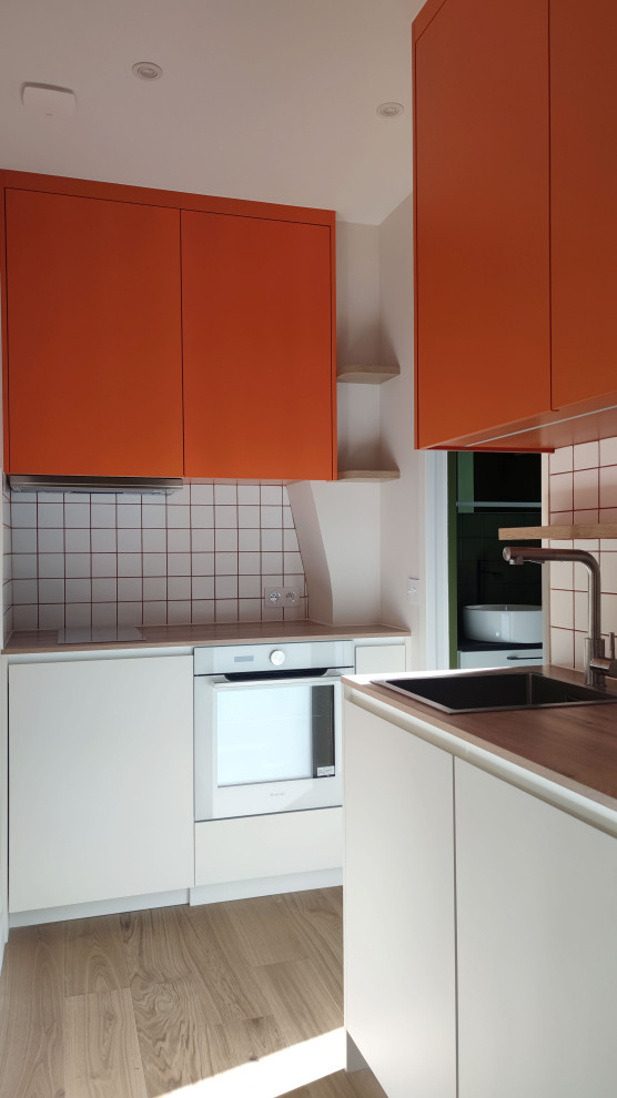 Photo of a mid-sized modern single-wall kitchen in Paris with a single-bowl sink, beaded inset cabinets, orange cabinets, laminate benchtops, white splashback, ceramic splashback, white appliances, light hardwood floors, multiple islands and brown benchtop.