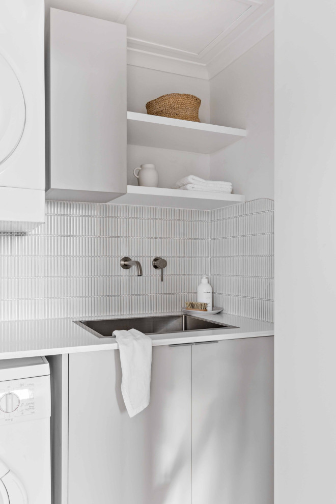 Inspiration för små moderna linjära vitt tvättstugor enbart för tvätt, med en nedsänkt diskho, släta luckor, grå skåp, bänkskiva i kvarts, vitt stänkskydd, stänkskydd i mosaik, vita väggar, klinkergolv i porslin, en tvättpelare och grått golv