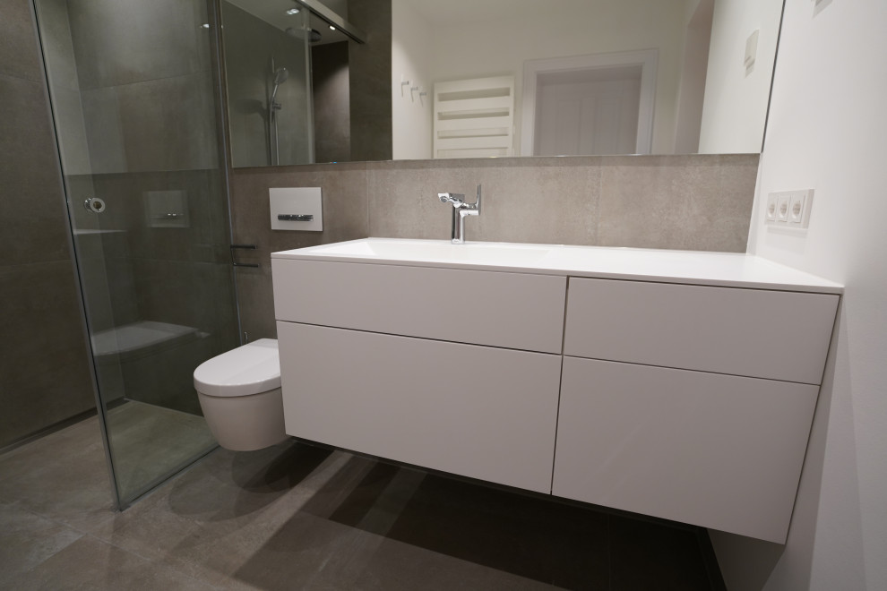 Exempel på ett mycket stort modernt vit vitt badrum med dusch, med släta luckor, vita skåp, en dusch i en alkov, en vägghängd toalettstol, grå kakel, vita väggar, ett integrerad handfat, bänkskiva i akrylsten, grått golv och dusch med skjutdörr