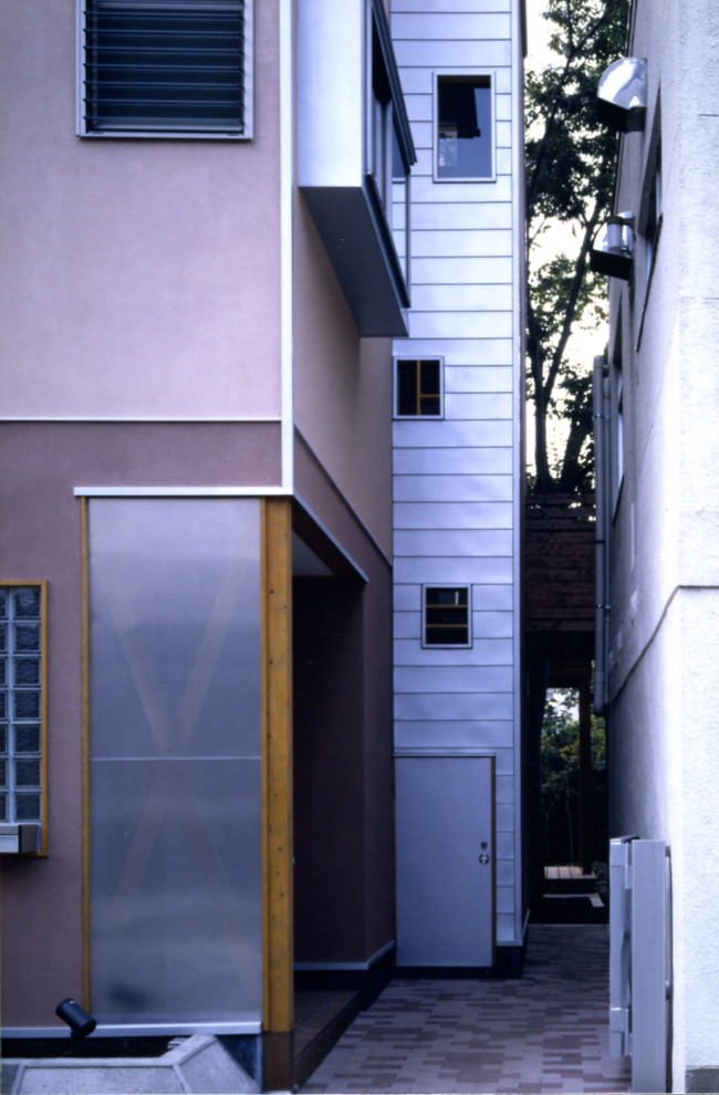 Photo of a mid-sized modern three-storey stucco orange house exterior in Other with a hip roof, a metal roof and a grey roof.