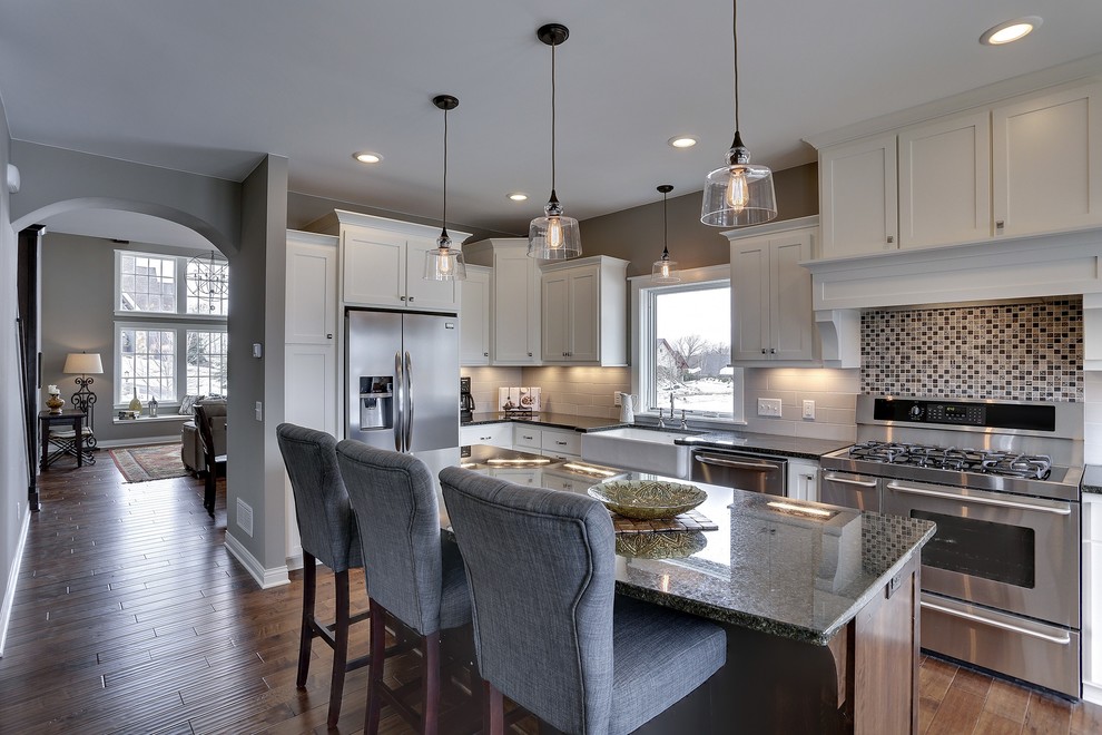 Photo of a mid-sized transitional l-shaped eat-in kitchen in Minneapolis with a farmhouse sink, shaker cabinets, white cabinets, laminate benchtops, grey splashback, ceramic splashback, stainless steel appliances, dark hardwood floors and with island.