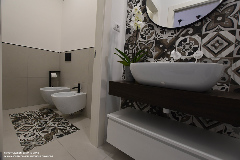 Cette image montre un petit WC et toilettes design avec un placard à porte plane, des portes de placard blanches, WC séparés, un carrelage multicolore, des carreaux de béton, un mur blanc, carreaux de ciment au sol, une vasque, un plan de toilette en bois, un sol multicolore, un plan de toilette marron et meuble-lavabo suspendu.