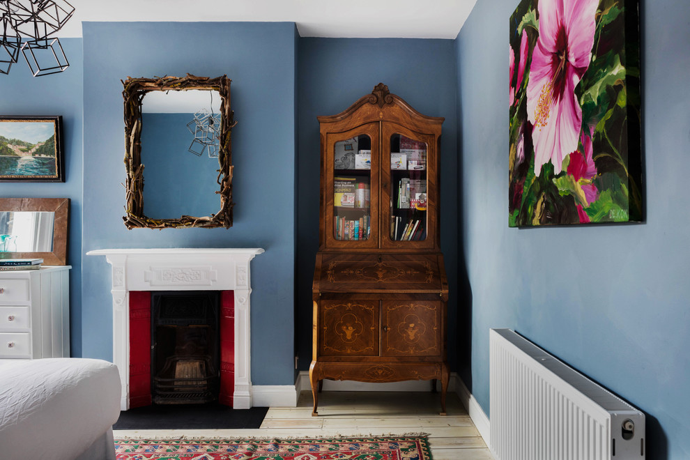 Design ideas for a mid-sized eclectic guest bedroom in London with blue walls, light hardwood floors, a standard fireplace and a wood fireplace surround.