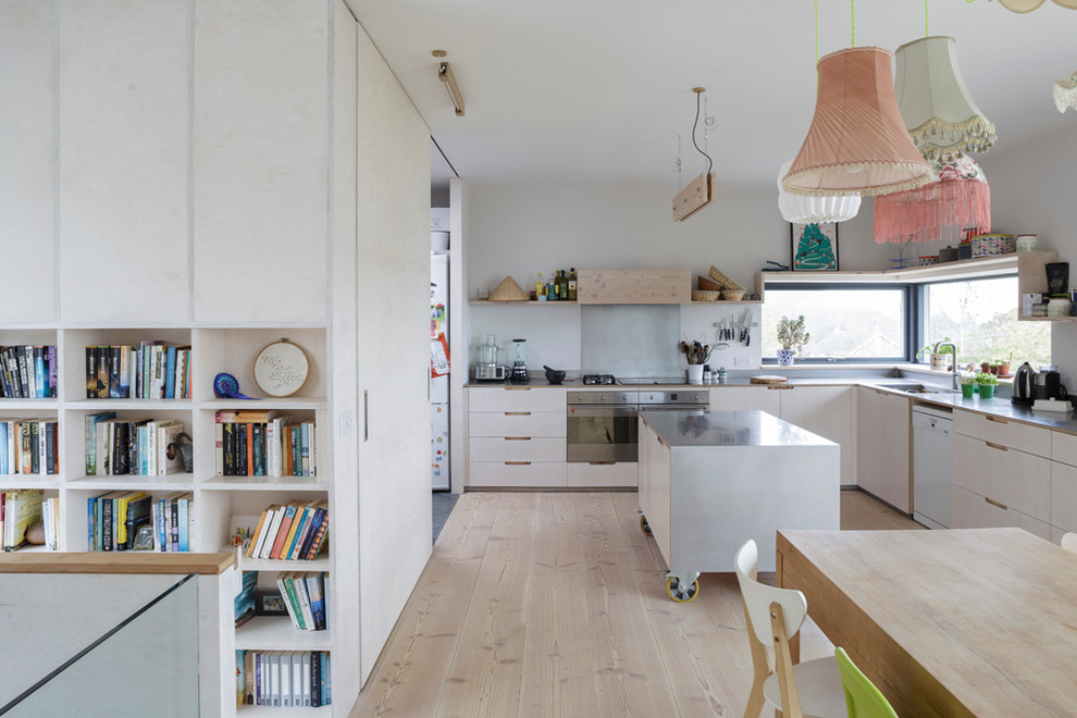 This is an example of a mid-sized eclectic l-shaped eat-in kitchen in Gloucestershire with flat-panel cabinets, white cabinets, stainless steel benchtops, with island, an integrated sink, white splashback, stainless steel appliances and painted wood floors.