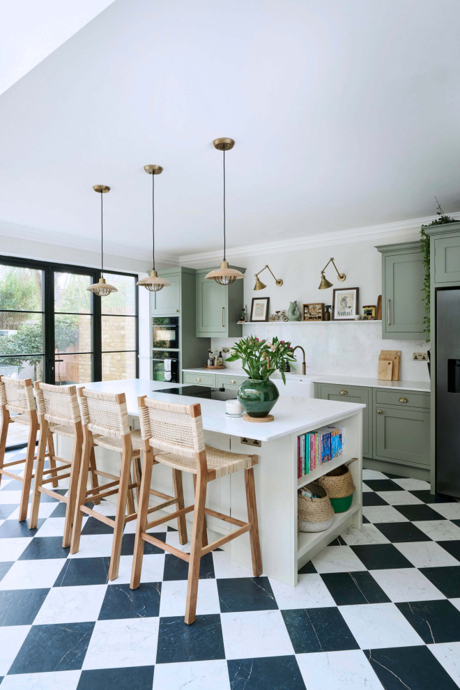 This is an example of a large victorian single-wall open plan kitchen in London with a single-bowl sink, shaker cabinets, green cabinets, quartz worktops, white splashback, black appliances, an island, multi-coloured floors and white worktops.