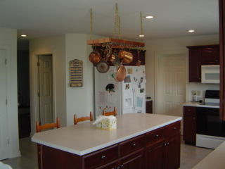 Kitchen - l-shaped ceramic tile and beige floor kitchen idea with recessed-panel cabinets, an island, dark wood cabinets, black appliances and white countertops