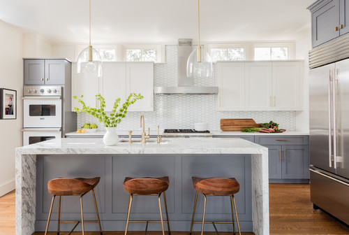 Bright kitchen with two-tone shaker Ready-to-Assemble (RTA) cabinets—white uppers and gray bases—brass hardware, marble waterfall island, hex tile backsplash, glass pendants, stainless appliances, and wood stools.