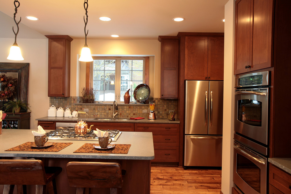Example of a mid-sized mountain style medium tone wood floor eat-in kitchen design in Seattle with a double-bowl sink, shaker cabinets, medium tone wood cabinets, granite countertops, stone tile backsplash, stainless steel appliances and an island
