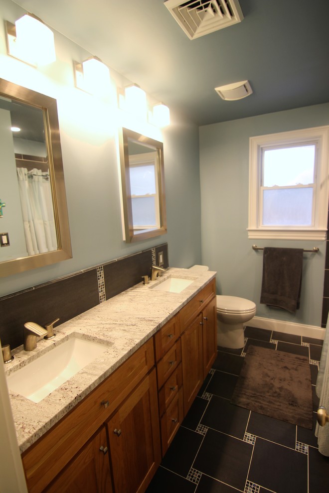 Photo of a mid-sized modern master bathroom in Baltimore with recessed-panel cabinets, medium wood cabinets, a shower/bathtub combo, a one-piece toilet, black tile, ceramic tile, blue walls, ceramic floors, an undermount sink and granite benchtops.