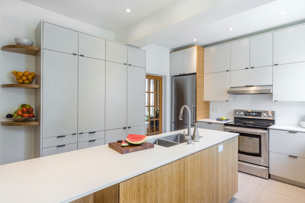 This is an example of a mid-sized transitional separate kitchen in Montreal with an undermount sink, flat-panel cabinets, light wood cabinets, solid surface benchtops, stainless steel appliances, linoleum floors, with island, beige floor and white benchtop.