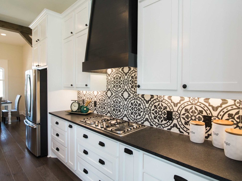Photo of a mid-sized country single-wall open plan kitchen in Austin with a farmhouse sink, flat-panel cabinets, white cabinets, black splashback, cement tile splashback, stainless steel appliances, laminate floors, with island, brown floor and white benchtop.