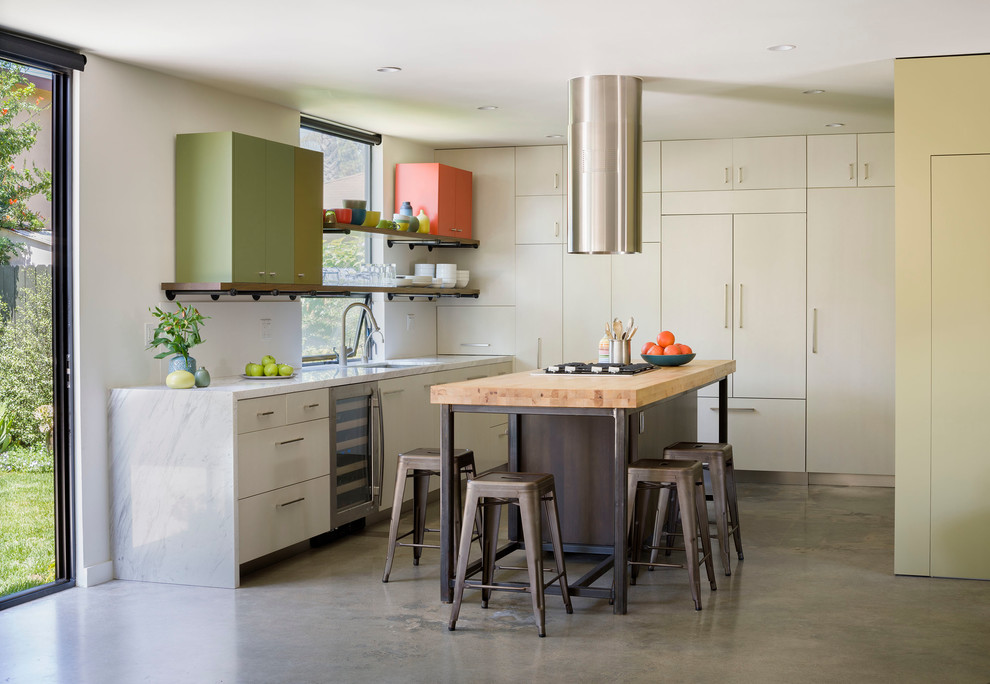 Small contemporary l-shaped eat-in kitchen in Los Angeles with an undermount sink, flat-panel cabinets, light wood cabinets, marble benchtops, white splashback, stone slab splashback, stainless steel appliances, concrete floors and with island.