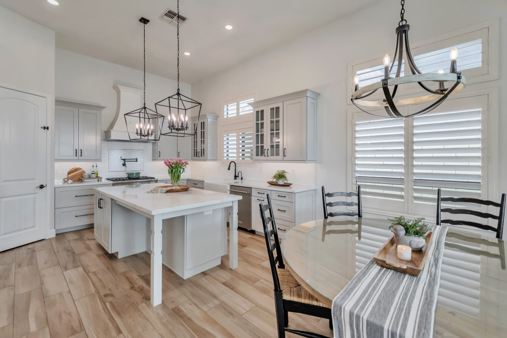 Large transitional u-shaped porcelain tile, brown floor and exposed beam kitchen photo in Phoenix with a farmhouse sink, shaker cabinets, gray cabinets, quartzite countertops, white backsplash, porcelain backsplash, stainless steel appliances, an island and white countertops