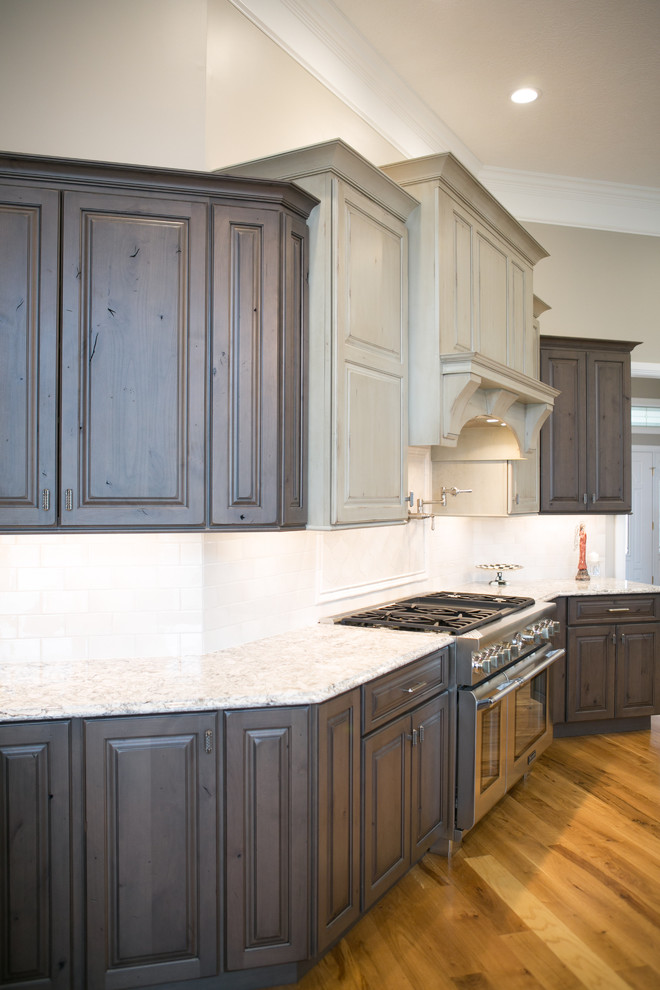 Kitchen - large transitional u-shaped medium tone wood floor and brown floor kitchen idea in Indianapolis with a farmhouse sink, raised-panel cabinets, dark wood cabinets, granite countertops, white backsplash, subway tile backsplash, paneled appliances, an island and multicolored countertops