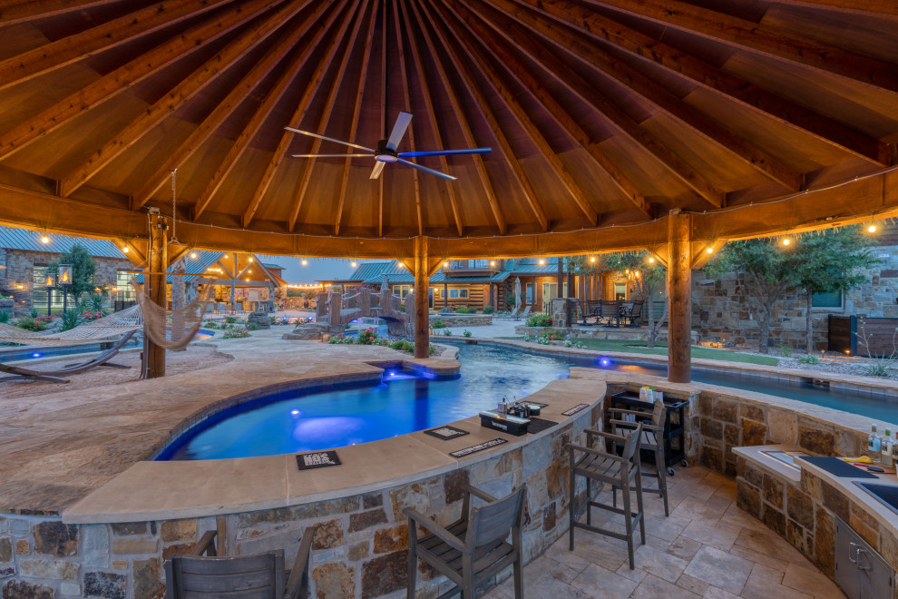 Imagen de piscina con tobogán rústica extra grande a medida en patio trasero con adoquines de piedra natural