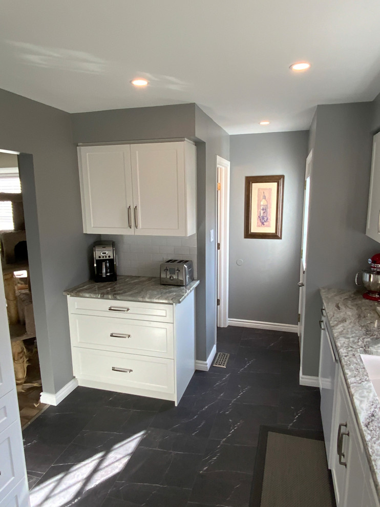 Example of a small transitional galley laminate floor and gray floor kitchen pantry design with an undermount sink, shaker cabinets, white cabinets, granite countertops, white backsplash, subway tile backsplash, white appliances, no island and white countertops