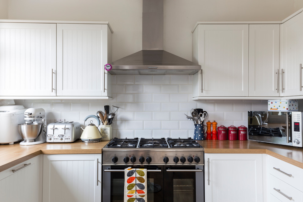 Photo of a contemporary u-shaped kitchen in London with shaker cabinets, white cabinets, wood benchtops, white splashback, subway tile splashback and stainless steel appliances.
