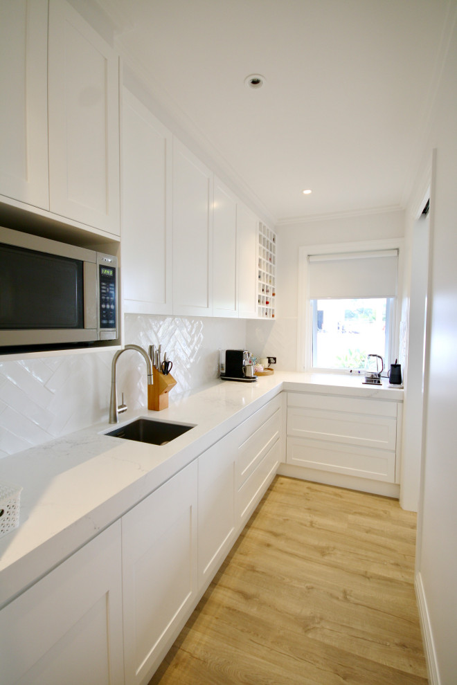 Inspiration for an expansive transitional u-shaped open plan kitchen in Sydney with an undermount sink, shaker cabinets, white cabinets, quartz benchtops, white splashback, subway tile splashback, stainless steel appliances, medium hardwood floors, with island, brown floor, white benchtop and recessed.