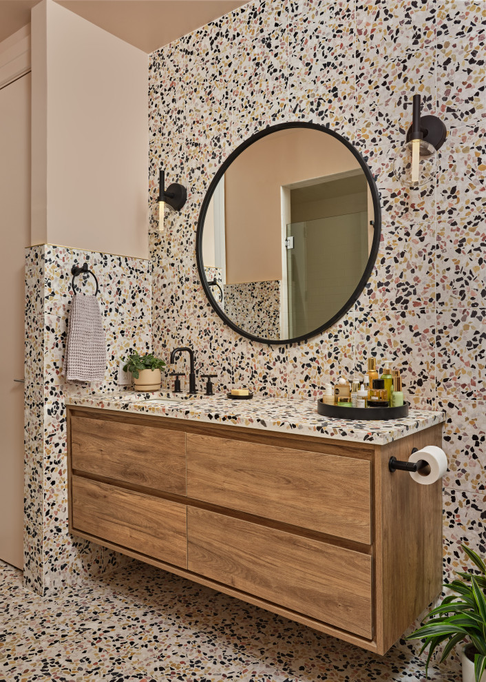 На фото: ванная комната в современном стиле с плоскими фасадами, фасадами цвета дерева среднего тона, разноцветной плиткой, розовыми стенами, полом из терраццо, врезной раковиной, разноцветным полом, тумбой под одну раковину и подвесной тумбой
