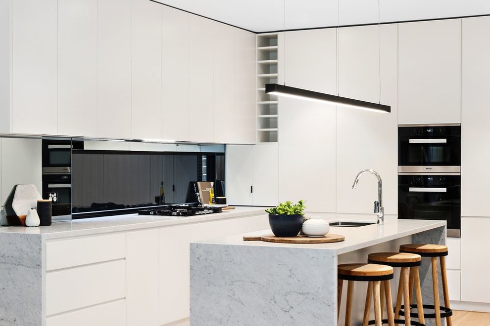 Inspiration for a mid-sized contemporary galley eat-in kitchen in Sydney with a double-bowl sink, flat-panel cabinets, white cabinets, quartz benchtops, glass sheet splashback, black appliances, light hardwood floors, with island and white benchtop.