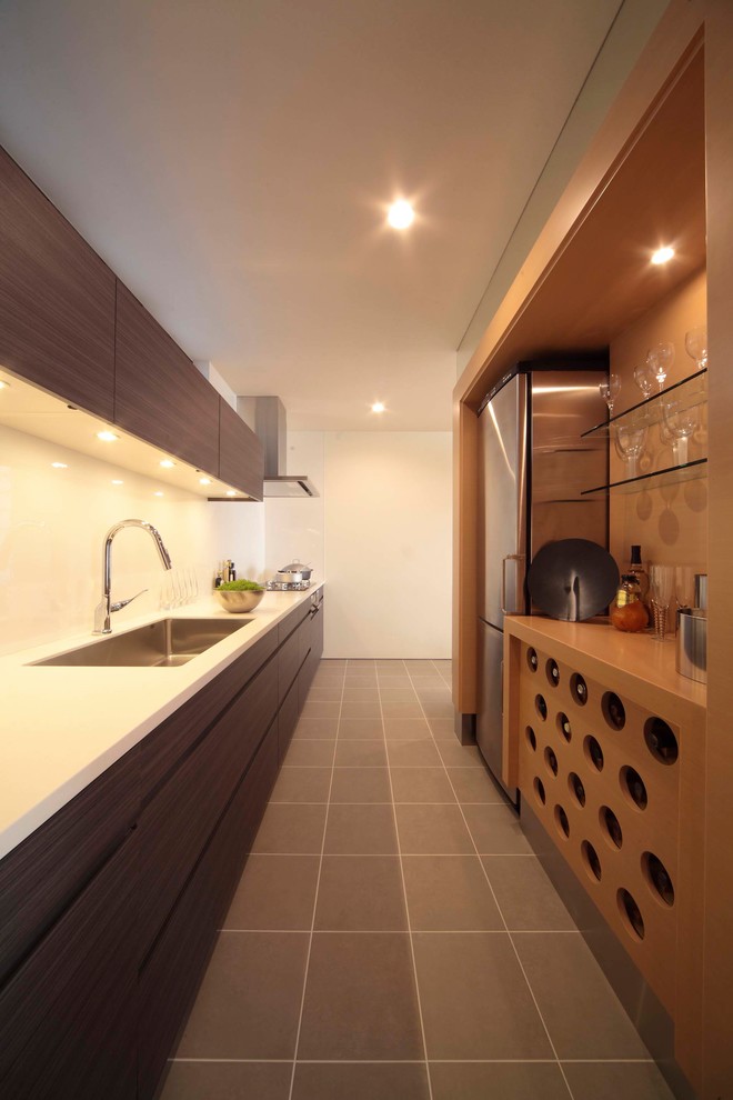 Photo of a modern galley kitchen in Tokyo with a single-bowl sink, flat-panel cabinets, dark wood cabinets, white splashback, grey floor and white benchtop.