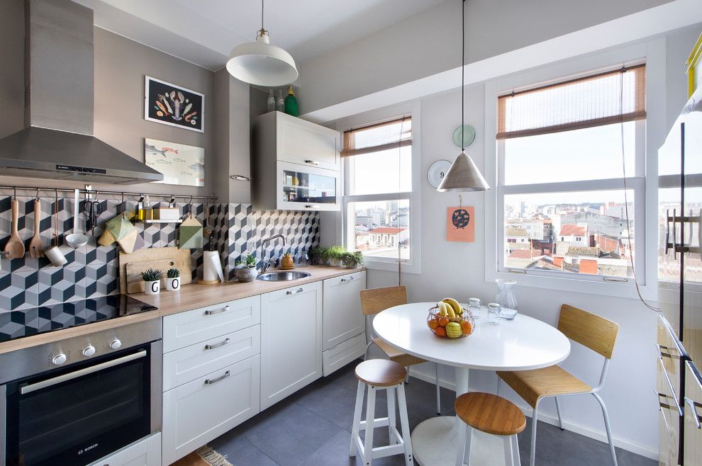 Mid-sized eclectic single-wall eat-in kitchen in Madrid with a single-bowl sink, recessed-panel cabinets, white cabinets, wood benchtops, multi-coloured splashback, ceramic splashback, stainless steel appliances, ceramic floors, no island and black floor.