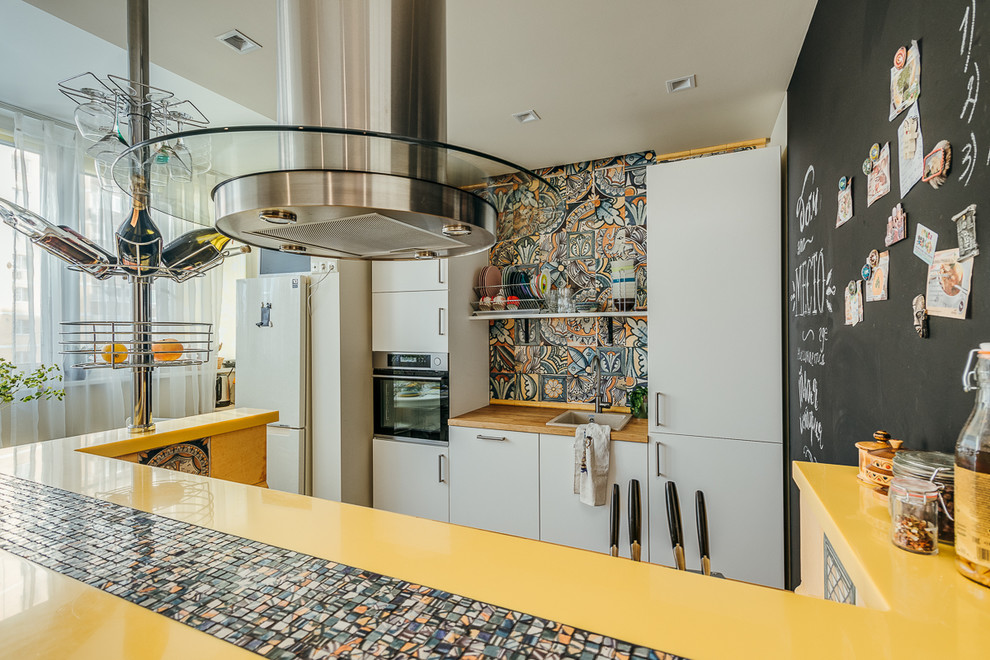 Design ideas for a small eclectic galley eat-in kitchen in Moscow with a drop-in sink, flat-panel cabinets, white cabinets, multi-coloured splashback, ceramic splashback, stainless steel appliances, medium hardwood floors, with island, brown floor and yellow benchtop.