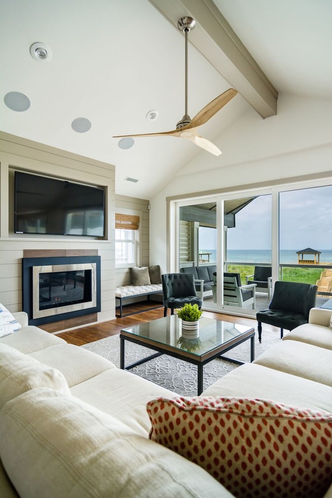 Mid-sized beach style formal open concept living room in Other with white walls, medium hardwood floors, a standard fireplace, a wood fireplace surround, a wall-mounted tv and brown floor.