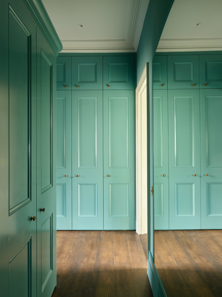 This is an example of a mid-sized traditional gender-neutral storage and wardrobe in London with beaded inset cabinets, blue cabinets, dark hardwood floors and brown floor.