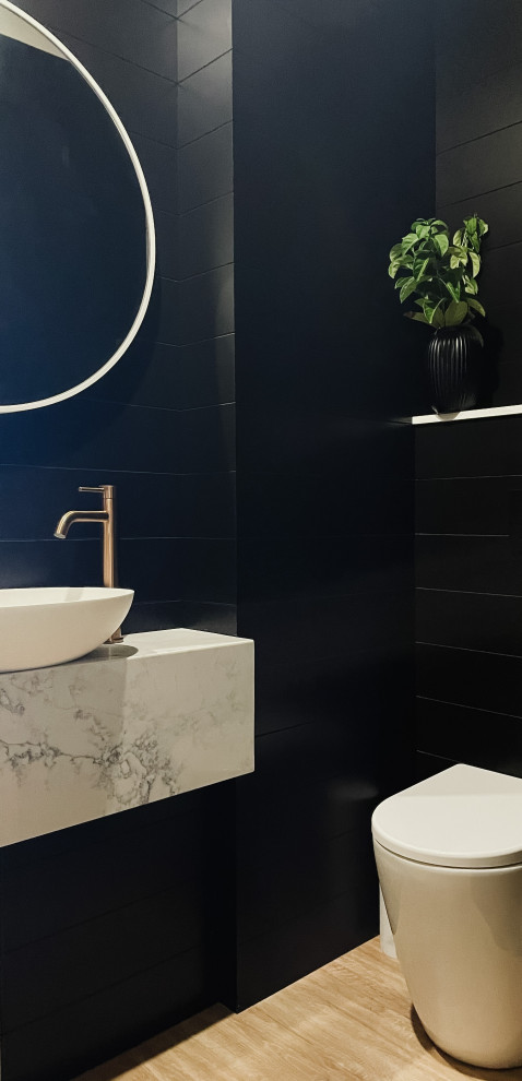 This is an example of a small contemporary powder room in Gold Coast - Tweed with white cabinets, a wall-mount toilet, black tile, black walls, light hardwood floors, a pedestal sink, marble benchtops, white benchtops, a floating vanity and planked wall panelling.
