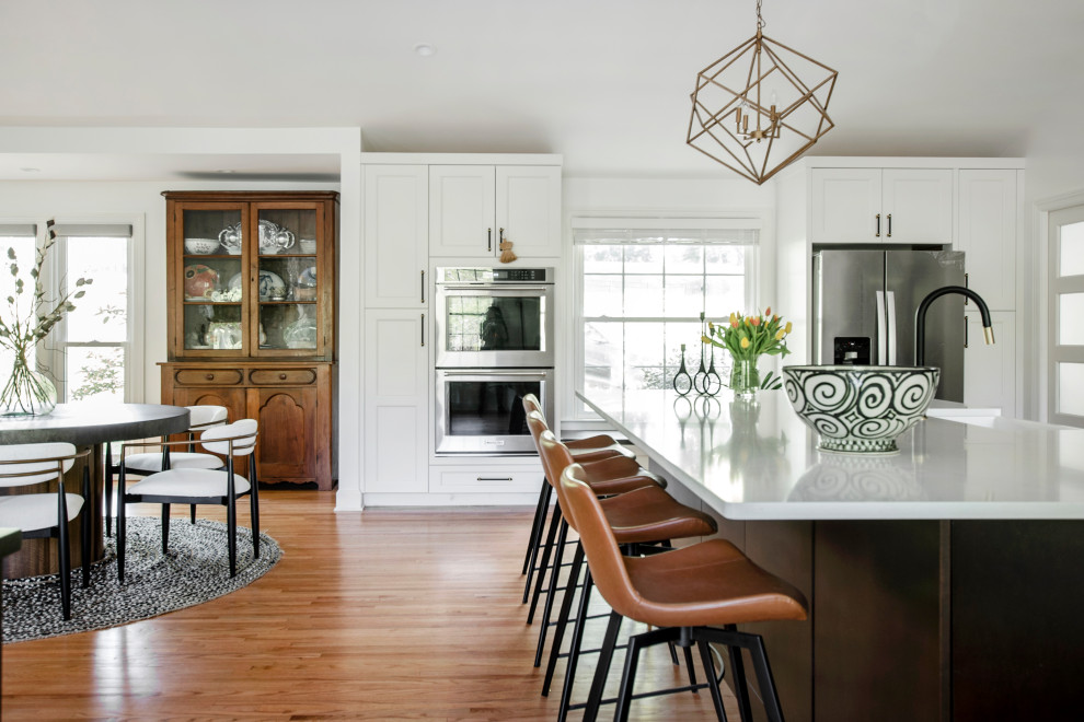 Design ideas for an expansive transitional u-shaped open plan kitchen in Nashville with an undermount sink, recessed-panel cabinets, white cabinets, quartz benchtops, white splashback, porcelain splashback, stainless steel appliances, medium hardwood floors, with island, brown floor, white benchtop and vaulted.