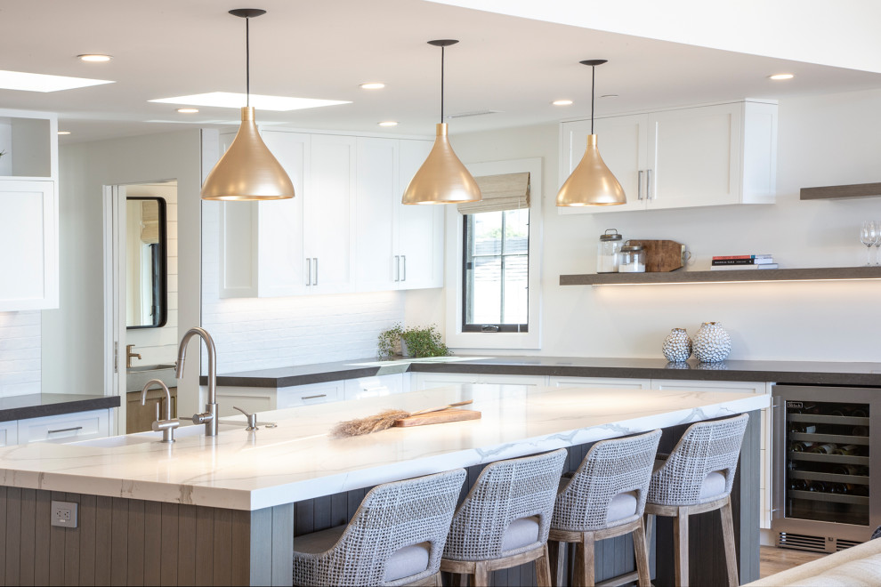 Transitional open concept kitchen photo in Orange County with a farmhouse sink, shaker cabinets, quartz countertops, white backsplash, brick backsplash, stainless steel appliances, an island and white countertops