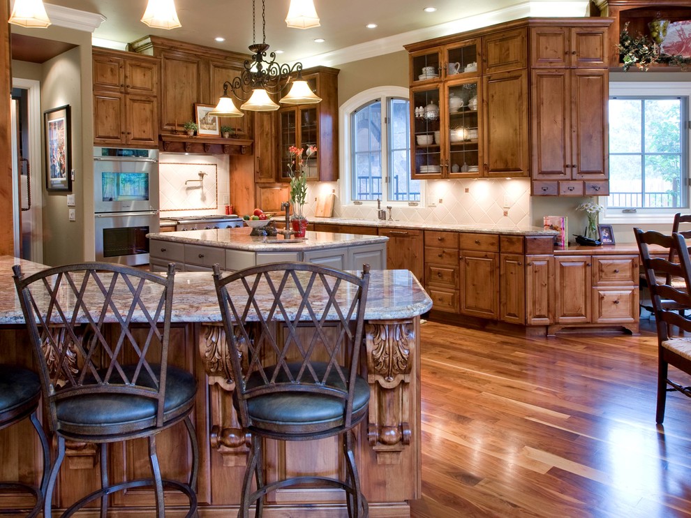 Design ideas for a large traditional l-shaped open plan kitchen in Portland with raised-panel cabinets, medium wood cabinets, granite benchtops, stainless steel appliances, light hardwood floors and multiple islands.