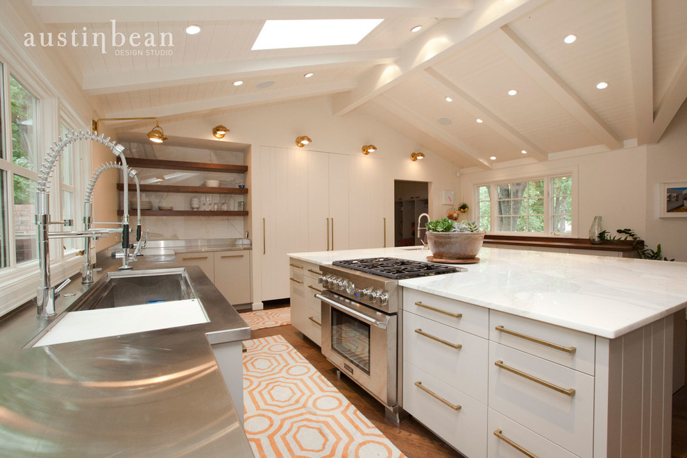 Inspiration for a large transitional u-shaped medium tone wood floor eat-in kitchen remodel with an integrated sink, flat-panel cabinets, white cabinets, stainless steel countertops, white backsplash, stone slab backsplash, stainless steel appliances and white walls