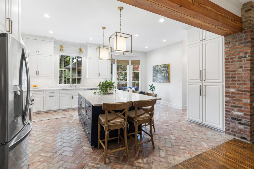 Inspiration for a large traditional l-shaped open plan kitchen in New Orleans with an undermount sink, raised-panel cabinets, white cabinets, quartzite benchtops, grey splashback, ceramic splashback, stainless steel appliances, brick floors, with island, red floor and grey benchtop.