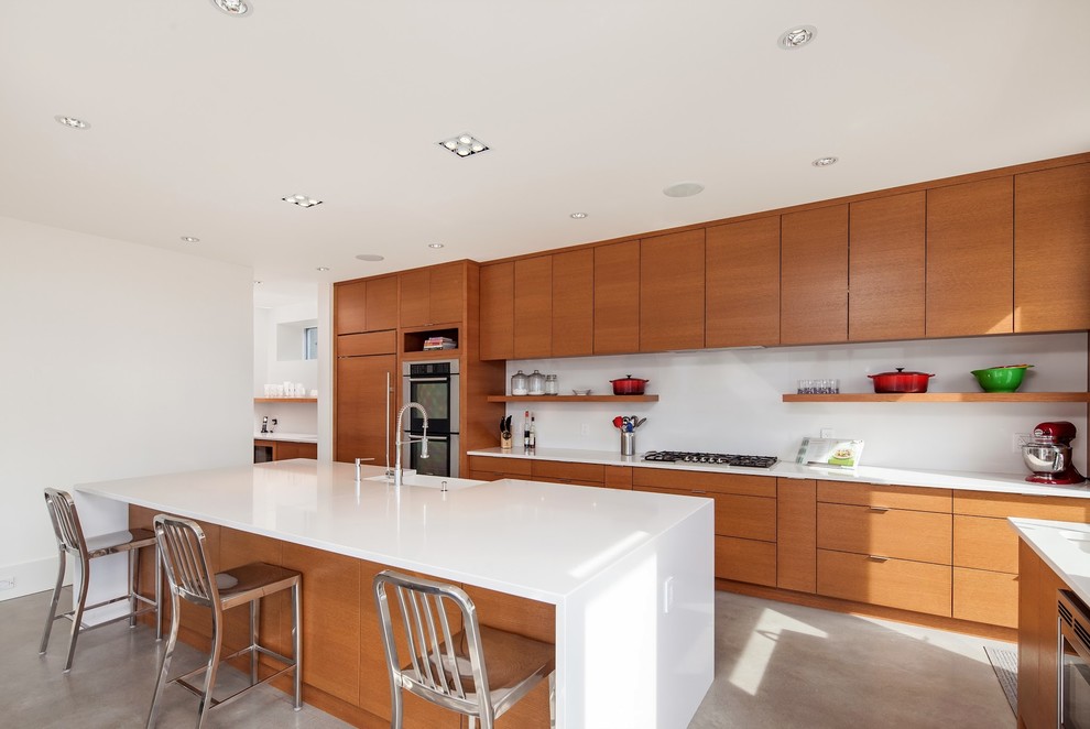 Photo of a mid-sized contemporary single-wall open plan kitchen in Vancouver with a farmhouse sink, flat-panel cabinets, medium wood cabinets, panelled appliances, quartzite benchtops, white splashback, concrete floors and with island.