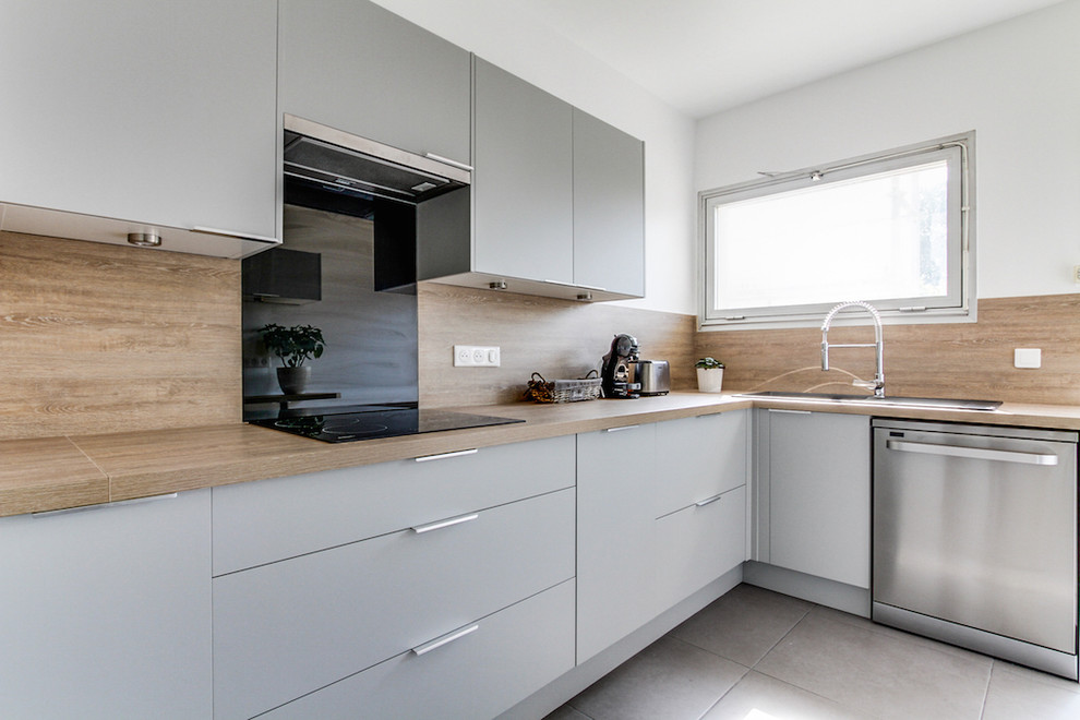 Cette image montre une grande cuisine nordique en L fermée avec un évier 1 bac, un placard à porte affleurante, des portes de placard grises, un plan de travail en stratifié, une crédence beige, un électroménager noir, un sol en carrelage de céramique, aucun îlot, un sol gris et un plan de travail beige.