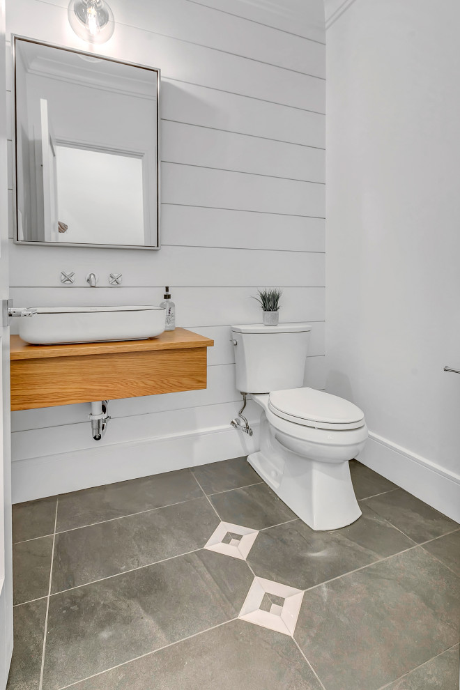 Inspiration for a small farmhouse cloakroom in New York with freestanding cabinets, medium wood cabinets, a two-piece toilet, white walls, porcelain flooring, a vessel sink, wooden worktops, grey floors, beige worktops and a floating vanity unit.