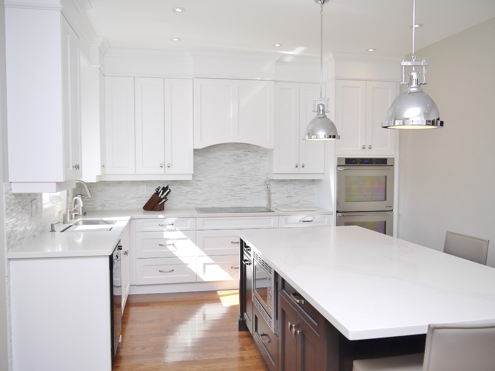 Mid-sized transitional l-shaped medium tone wood floor eat-in kitchen photo in Toronto with an undermount sink, recessed-panel cabinets, white cabinets, quartz countertops, white backsplash, stone tile backsplash, stainless steel appliances and an island
