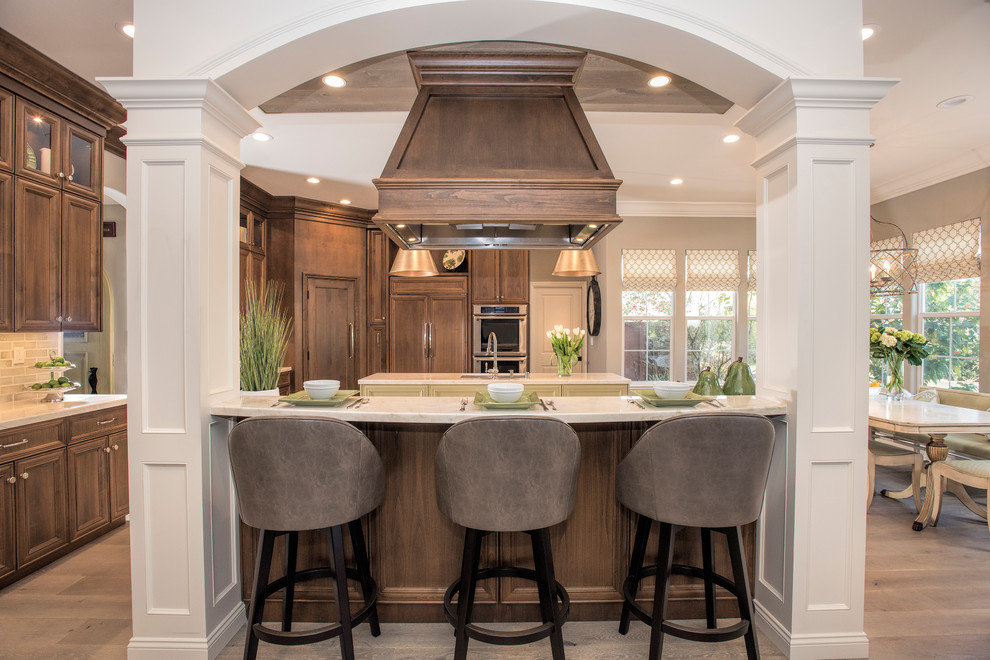 Inspiration for a large transitional l-shaped eat-in kitchen in San Francisco with an undermount sink, recessed-panel cabinets, quartzite benchtops, glass tile splashback, panelled appliances, multiple islands, dark wood cabinets, medium hardwood floors, beige floor and beige benchtop.