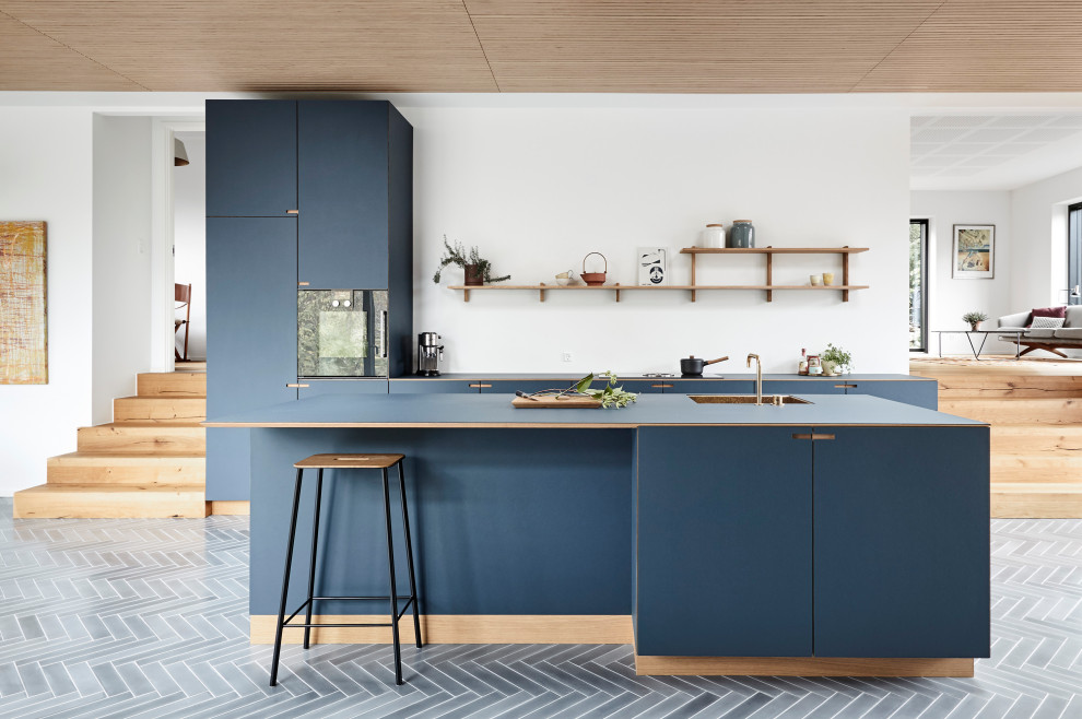 Large contemporary galley open plan kitchen in Copenhagen with flat-panel cabinets, blue cabinets, panelled appliances, with island, grey floor, blue benchtop and cement tiles.
