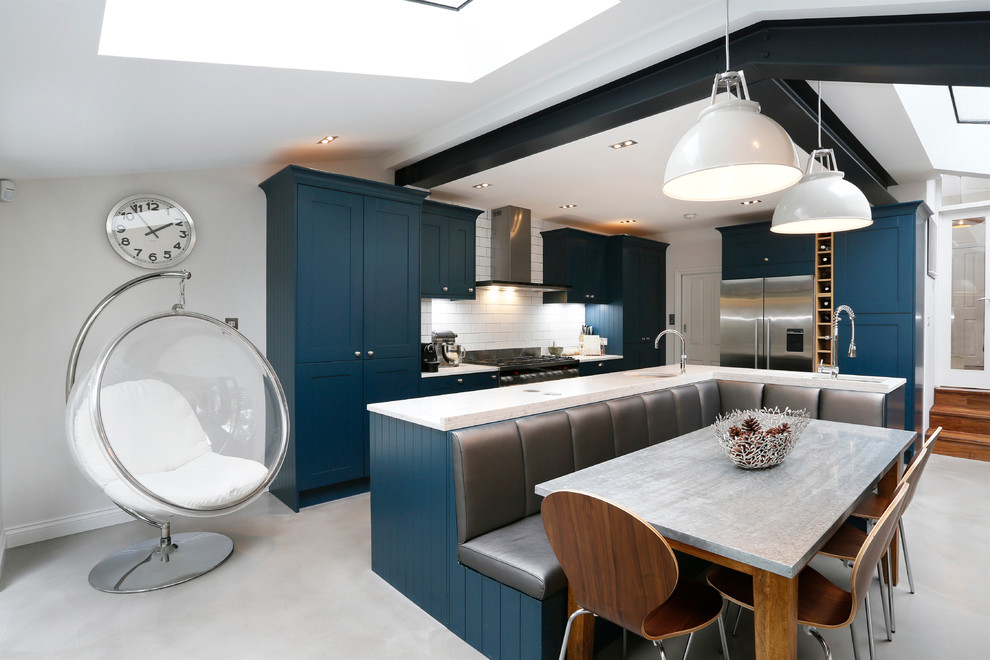 This is an example of a transitional l-shaped eat-in kitchen in London with an undermount sink, shaker cabinets, blue cabinets, white splashback, subway tile splashback, stainless steel appliances and with island.